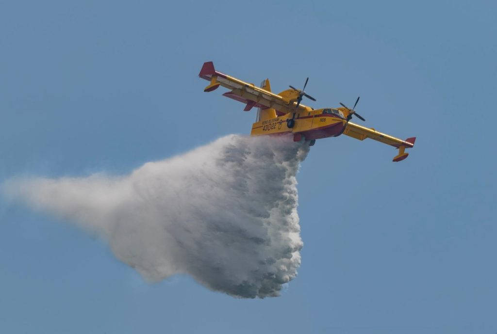 Aeronave de combate a incêndios despeja água sobre uma área em chamas durante uma operação de emergência.