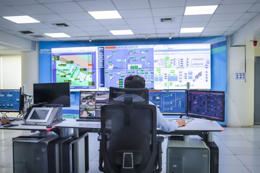 Operador acompanha sistemas tecnológicos em uma moderna sala de controle.
