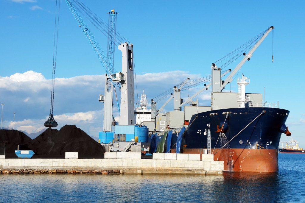 Porto de Ilhéus registra alta de 71,44% nas cargas exportadas em agosto Navio cargueiro e guindastes operam em um terminal portuário industrial durante o carregamento de minerais.