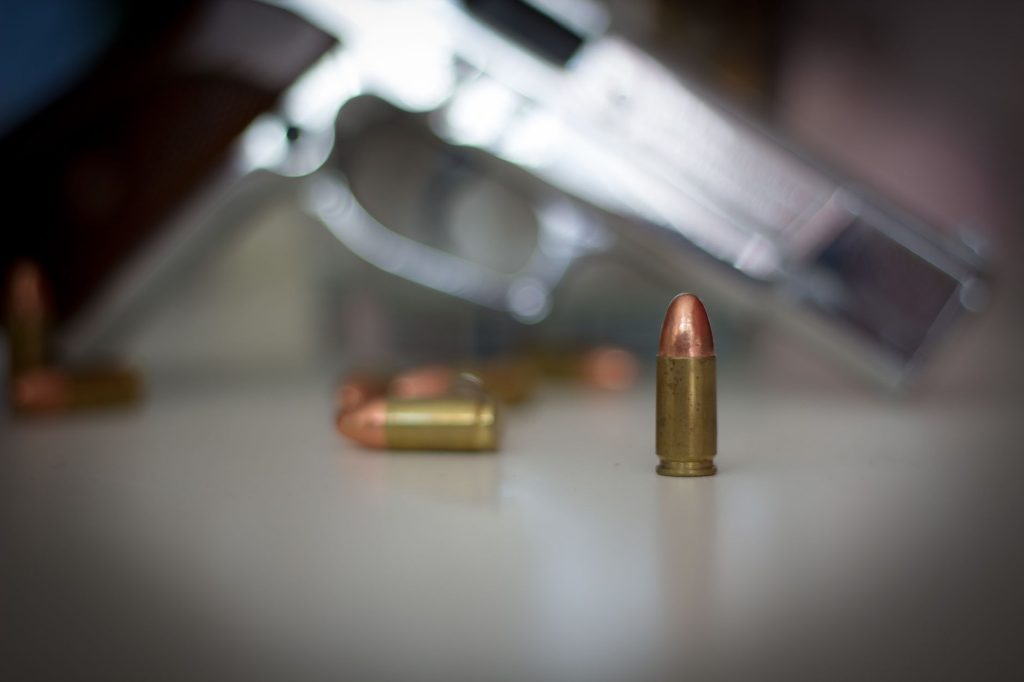 PF deflagra Operação Magen contra tráfico de armas, vazamento de dados e lavagem de dinheiro no Rio Close de uma munição em primeiro plano, com uma pistola desfocada ao fundo.